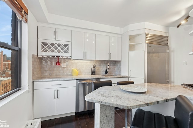 330 3rd Ave Unit 12B, New York City, NY 10010 - kitchen with appliances with stainless steel finishes, tasteful backsplash, white cabinets, dark wood-style floors, and a kitchen breakfast bar