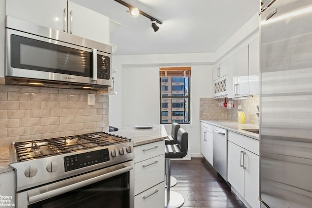 330 3rd Ave Unit 12B, New York City, NY 10010 - kitchen featuring appliances with stainless steel finishes, white cabinetry, dark wood-style floors, backsplash, and light stone counters