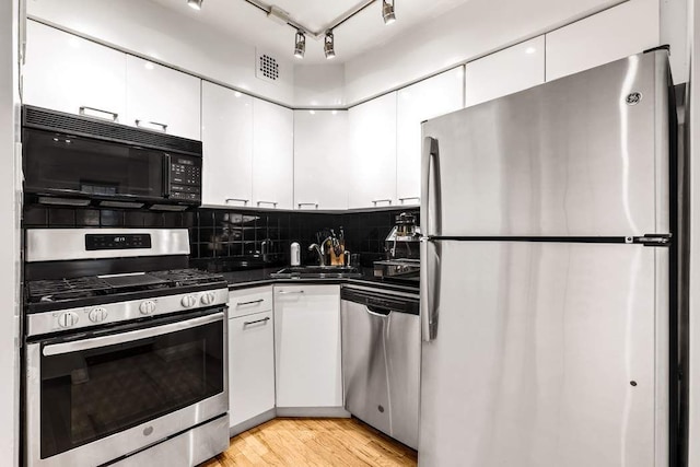 314 E 50th St Unit 1E, New York City, NY 10022 - kitchen featuring appliances with stainless steel finishes, a sink, white cabinetry, dark countertops, and backsplash