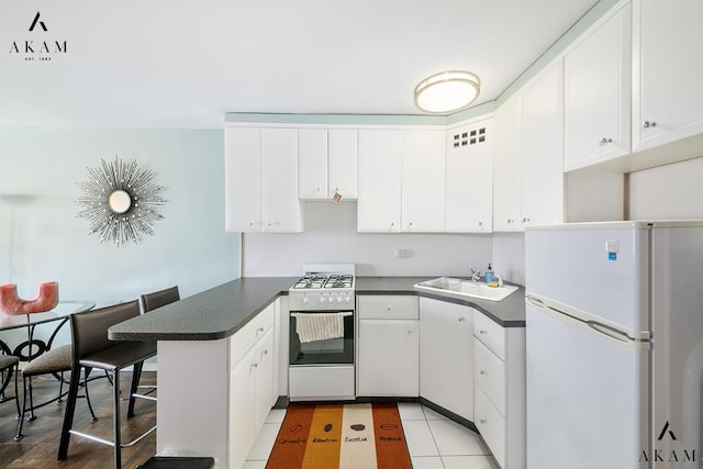 155 E 38th St Unit 9-H, New York City, NY 10016 - kitchen featuring white appliances, a sink, a peninsula, dark countertops, and white cabinets
