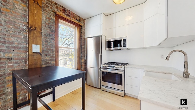 467 Pacific St Unit 18, New York City, NY 11217 - kitchen featuring stainless steel appliances, light wood-style floors, white cabinetry, light stone counters, and brick wall