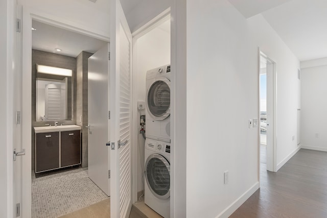 clothes washing area with baseboards, laundry area, stacked washer / dryer, and light wood-type flooring