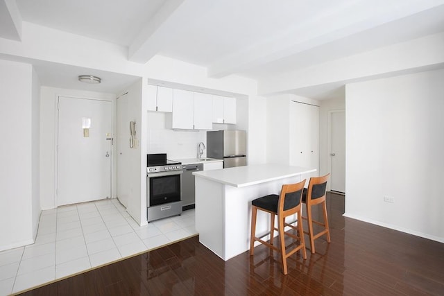 kitchen featuring a sink, beam ceiling, a kitchen breakfast bar, white cabinets, and appliances with stainless steel finishes