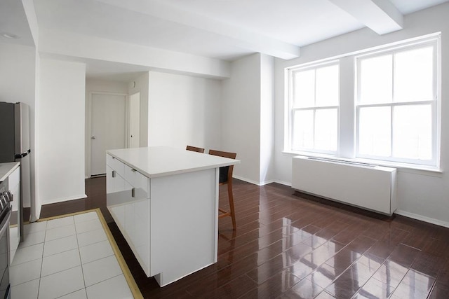 kitchen featuring baseboards, a breakfast bar, radiator heating unit, beam ceiling, and a center island