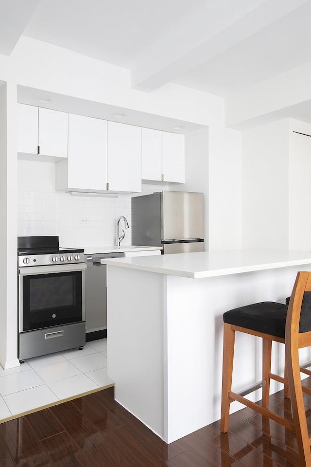 kitchen with a breakfast bar area, decorative backsplash, white cabinets, appliances with stainless steel finishes, and light countertops