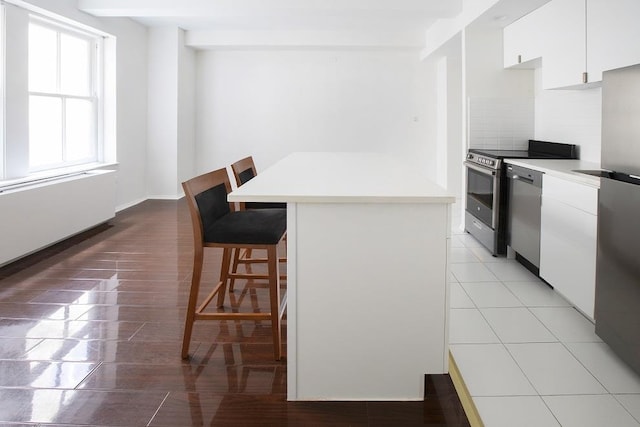 kitchen with a breakfast bar, appliances with stainless steel finishes, light countertops, white cabinets, and light wood-type flooring