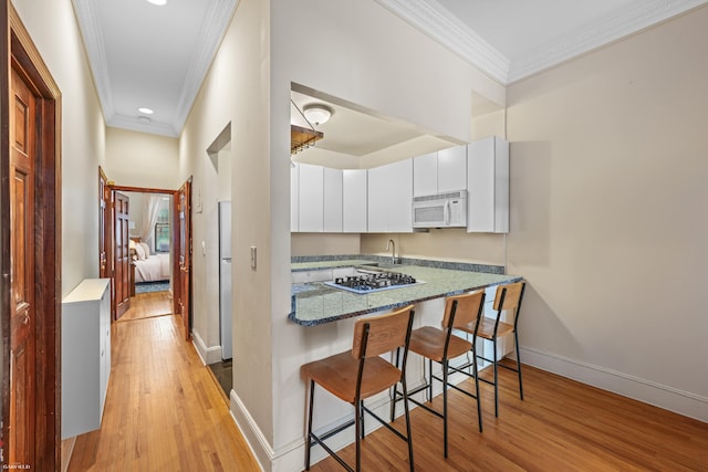 489 W End Ave, New York City, NY 10024 - kitchen with white appliances, crown molding, light wood-style flooring, a breakfast bar area, and white cabinetry
