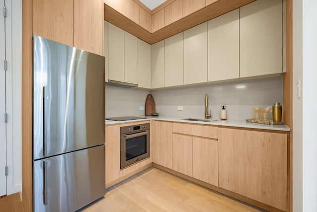 kitchen with appliances with stainless steel finishes, a sink, light countertops, light brown cabinetry, and light wood finished floors