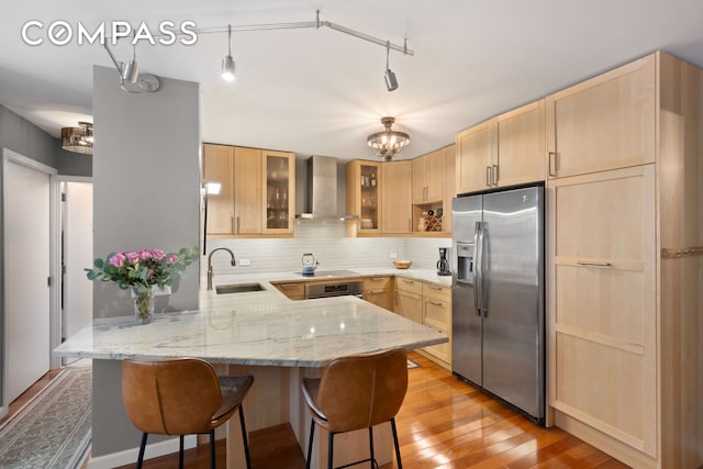 137 E 36th St Unit 8H, New York City, NY 10016 - kitchen featuring appliances with stainless steel finishes, wall chimney range hood, light brown cabinetry, and a peninsula