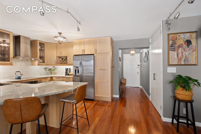137 E 36th St Unit 8H, New York City, NY 10016 - kitchen with wall chimney range hood, stainless steel refrigerator with ice dispenser, light brown cabinets, decorative backsplash, and light stone countertops
