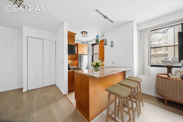 kitchen with stainless steel refrigerator, a peninsula, a breakfast bar, light wood-style flooring, and brown cabinets