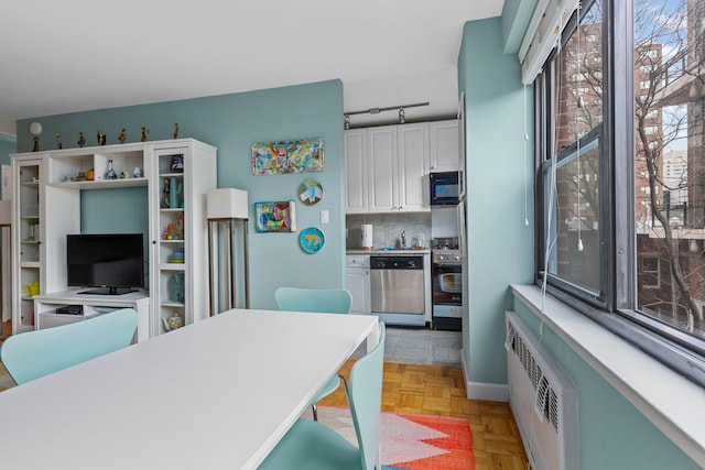 kitchen featuring radiator heating unit, tasteful backsplash, dishwasher, and white cabinetry