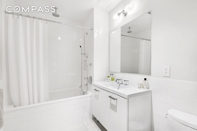 bathroom with vanity, toilet, tiled shower / bath combo, and tile walls