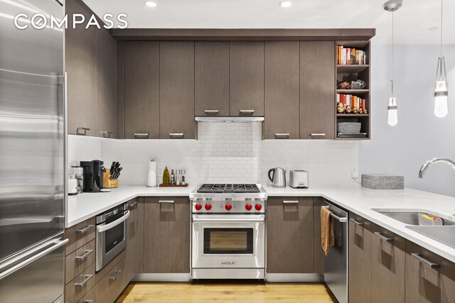 kitchen featuring dark brown cabinetry, a sink, high end appliances, and light countertops