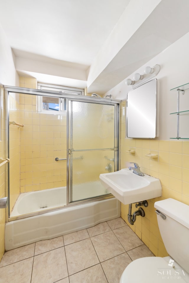 bathroom with toilet, tile patterned flooring, shower / bath combination with glass door, tile walls, and a sink