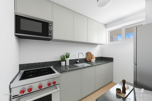 kitchen with appliances with stainless steel finishes, a sink, white cabinets, dark stone counters, and light tile patterned flooring