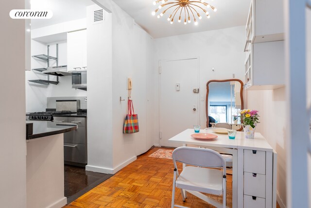 210 E 15th St Unit 1A, New York City, NY 10003 - kitchen featuring white cabinetry, a chandelier, dark countertops, stainless steel microwave, and baseboards