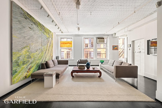 living room featuring baseboards, rail lighting, hardwood / wood-style flooring, and a wall mounted air conditioner
