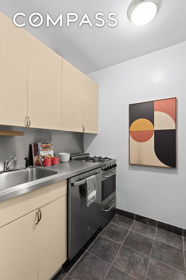 kitchen with appliances with stainless steel finishes, a sink, cream cabinetry, light countertops, and baseboards