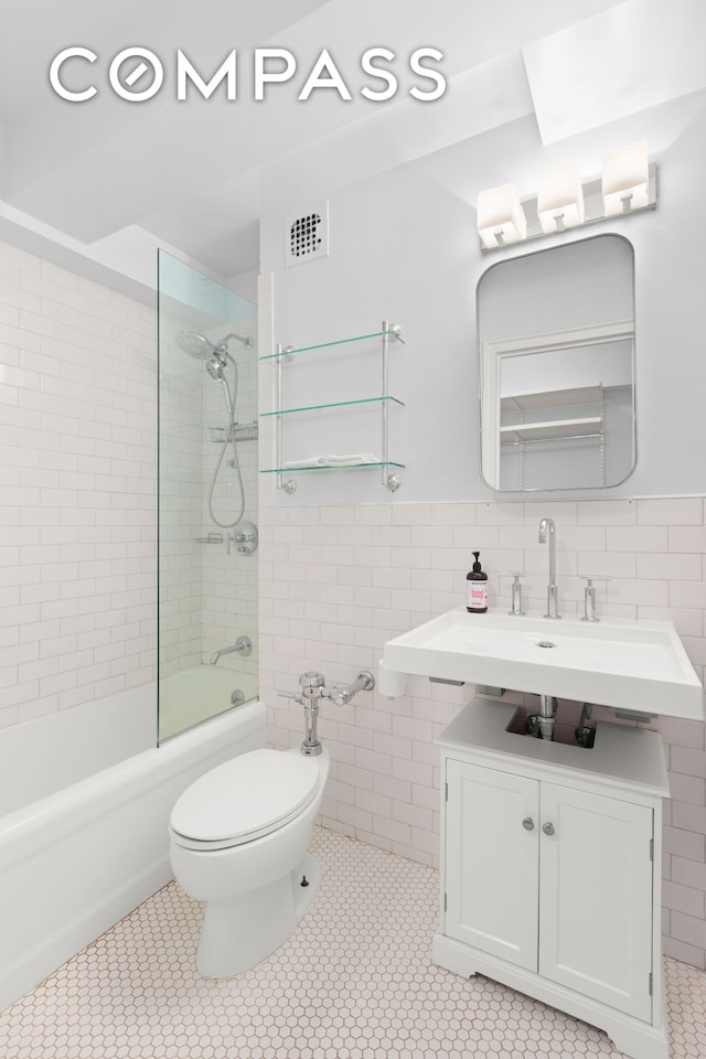 bathroom featuring tile walls, washtub / shower combination, a sink, toilet, and wainscoting
