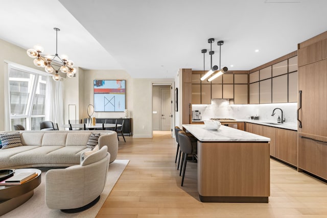 kitchen featuring an inviting chandelier, a sink, light wood-style floors, a kitchen island, and decorative backsplash