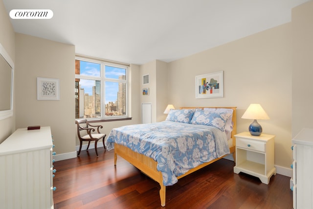 bedroom with dark wood finished floors, baseboards, and a city view