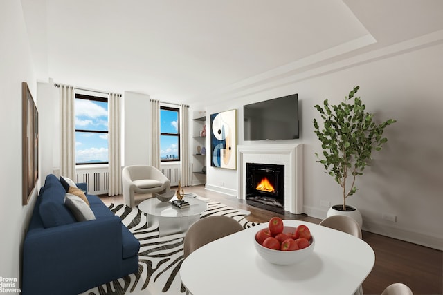 living area with radiator, wood finished floors, a fireplace with flush hearth, and built in shelves