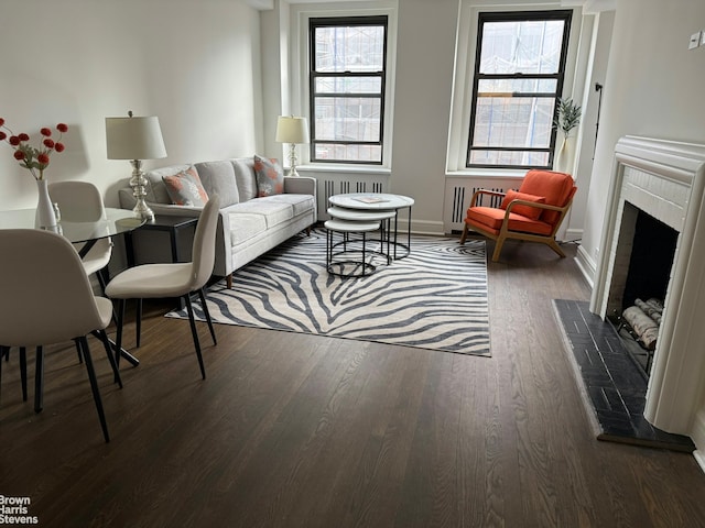 living area with dark wood-style floors, a brick fireplace, healthy amount of natural light, and baseboards