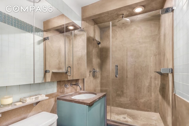 bathroom with tile walls, a stall shower, toilet, vanity, and backsplash