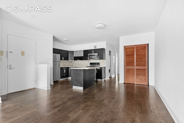 kitchen featuring stainless steel appliances, dark cabinetry, light countertops, a kitchen island, and decorative backsplash
