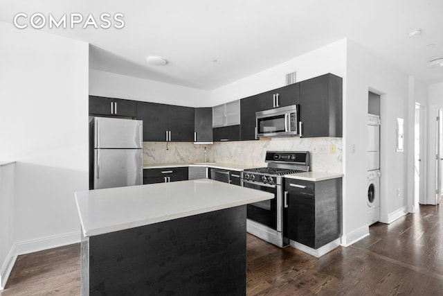 kitchen with appliances with stainless steel finishes, stacked washing machine and dryer, dark cabinetry, and decorative backsplash