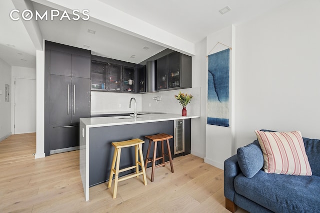 bar with a sink, beverage cooler, baseboards, light wood-type flooring, and tasteful backsplash
