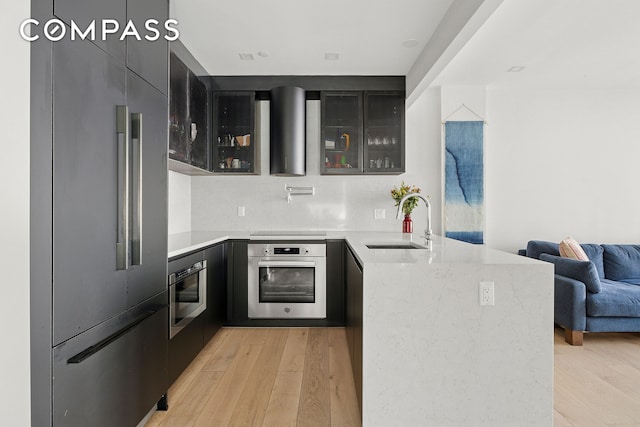 kitchen with appliances with stainless steel finishes, a sink, light wood-style floors, a peninsula, and glass insert cabinets