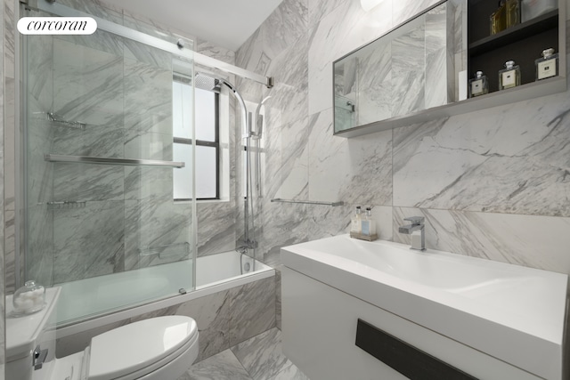 full bathroom with toilet, bath / shower combo with glass door, vanity, tile walls, and marble finish flooring