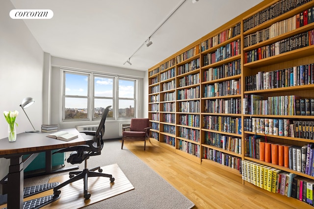 office space featuring wall of books, rail lighting, and wood finished floors