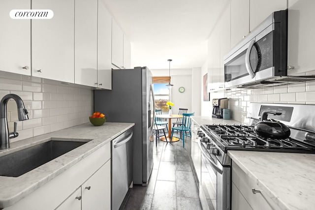 kitchen featuring appliances with stainless steel finishes, a sink, decorative backsplash, and white cabinetry