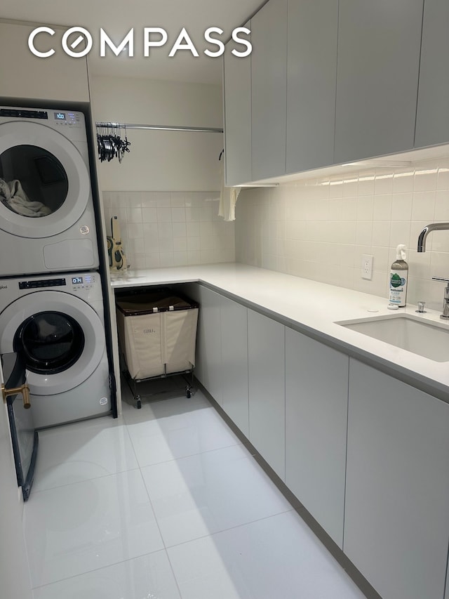 laundry area with stacked washing maching and dryer, cabinet space, light tile patterned flooring, and a sink