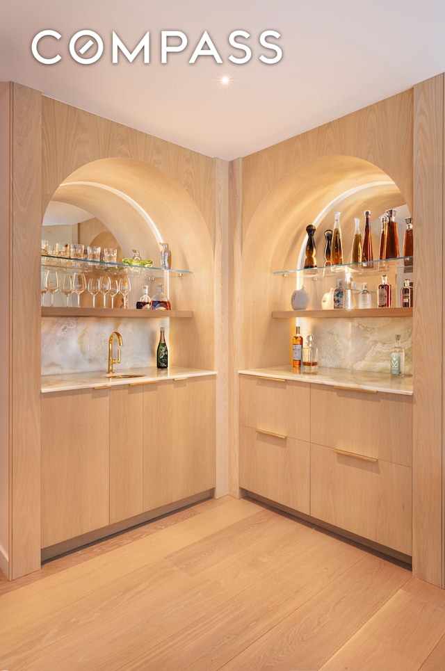 bar featuring light wood finished floors, indoor wet bar, and a sink