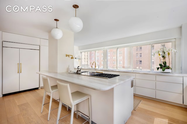 kitchen featuring paneled refrigerator, a breakfast bar, light wood-style floors, stainless steel cooktop, and white cabinetry