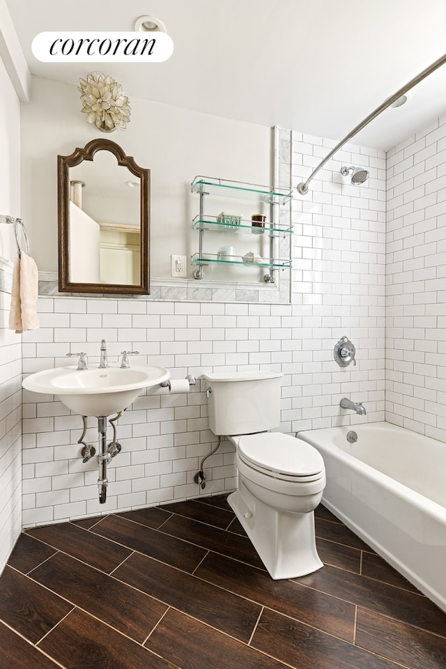 full bath with wood finish floors, toilet, shower / bath combination, tile walls, and a sink
