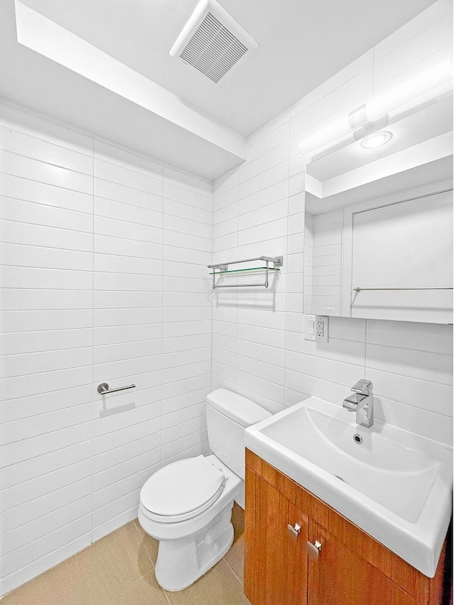 half bath with toilet, tile walls, visible vents, and vanity