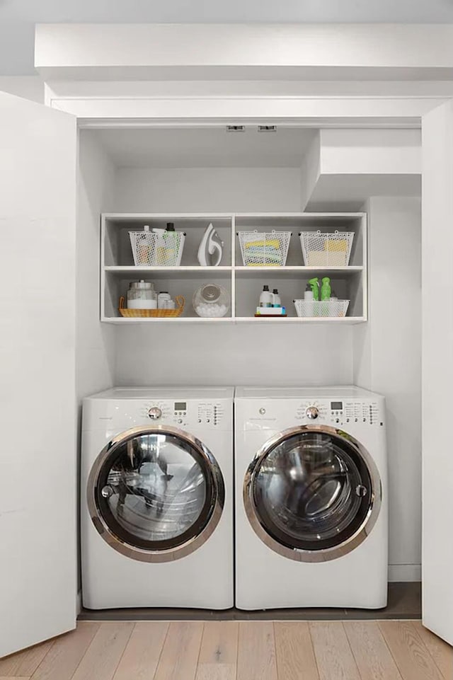 laundry area with laundry area, washing machine and dryer, and light wood-type flooring