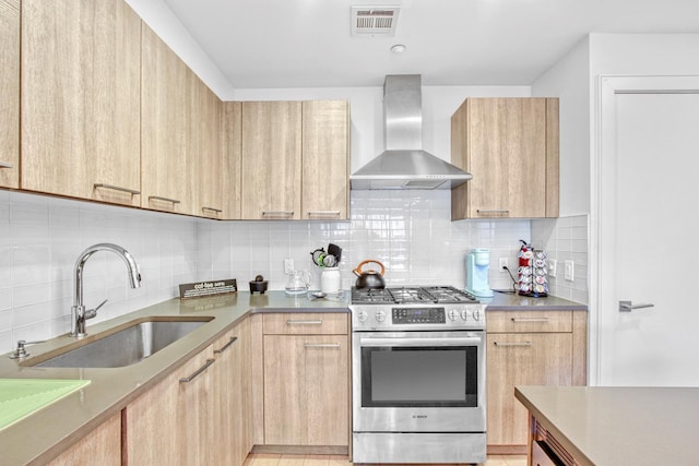 kitchen featuring visible vents, light brown cabinets, gas range, wall chimney exhaust hood, and a sink