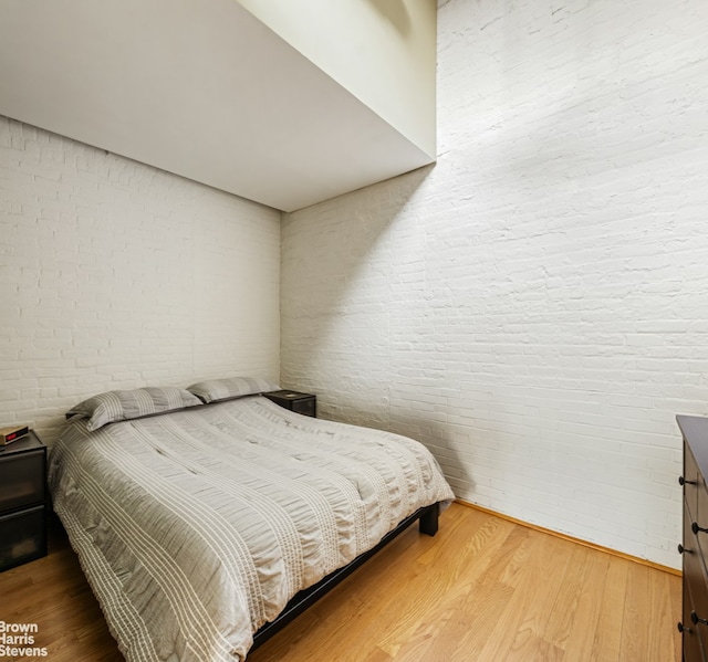 bedroom with wood finished floors and brick wall