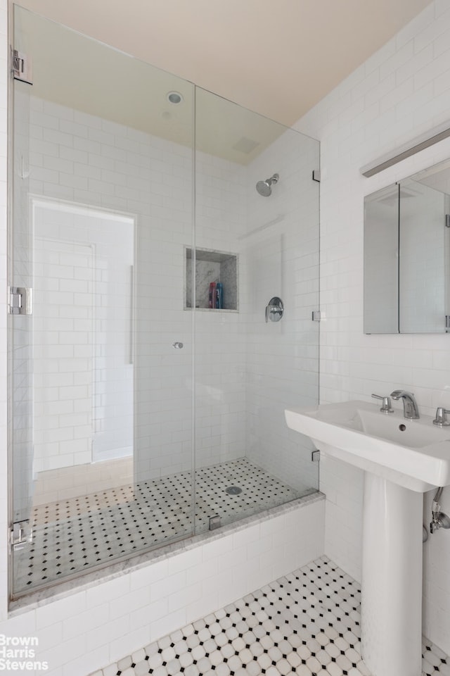 bathroom with a shower stall, tile walls, tile patterned floors, and a sink