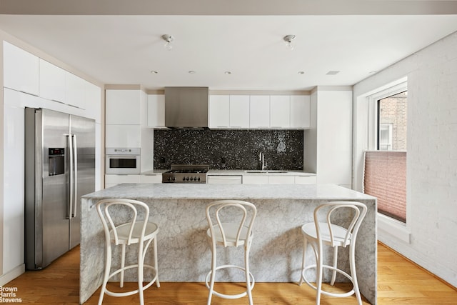 kitchen featuring stainless steel fridge, wall chimney range hood, white oven, modern cabinets, and a sink
