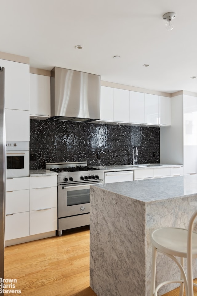kitchen with white appliances, modern cabinets, range hood, white cabinets, and light wood-style floors