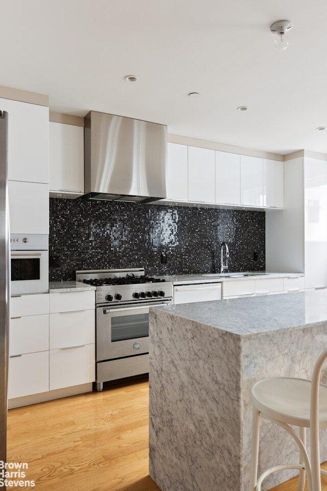 1 Worth St Unit 6R, New York City, NY 10013 - kitchen featuring stainless steel appliances, extractor fan, modern cabinets, white cabinetry, and light wood-style floors
