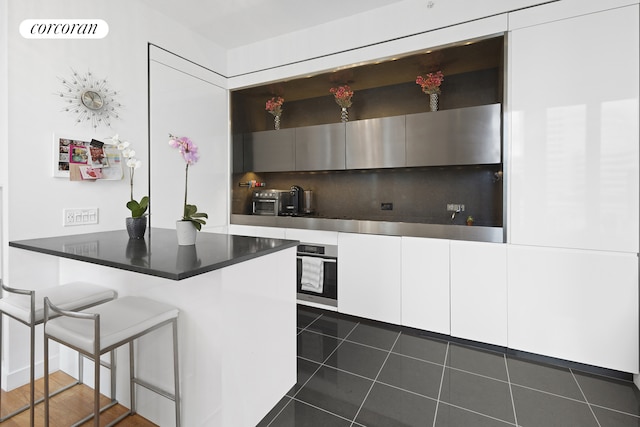15 William St Unit 23A, New York City, NY 10005 - kitchen with oven, a breakfast bar area, a peninsula, white cabinets, and dark tile patterned flooring