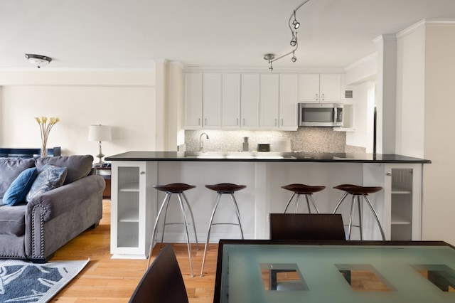 kitchen featuring stainless steel microwave, a breakfast bar, open floor plan, white cabinetry, and light wood-type flooring